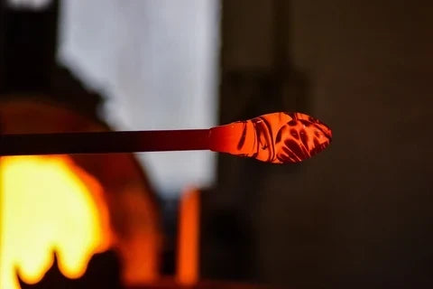 Molten glass glowing on the end of a blowpipe at the furnace